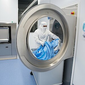 Waschmaschinen haben eine Durchladefunktion zum sicheren Einschleusen der Textilien. sie werden durch einen Mitarbeiter in Schutzkleidung befülltReinigung im Reinraum entladen