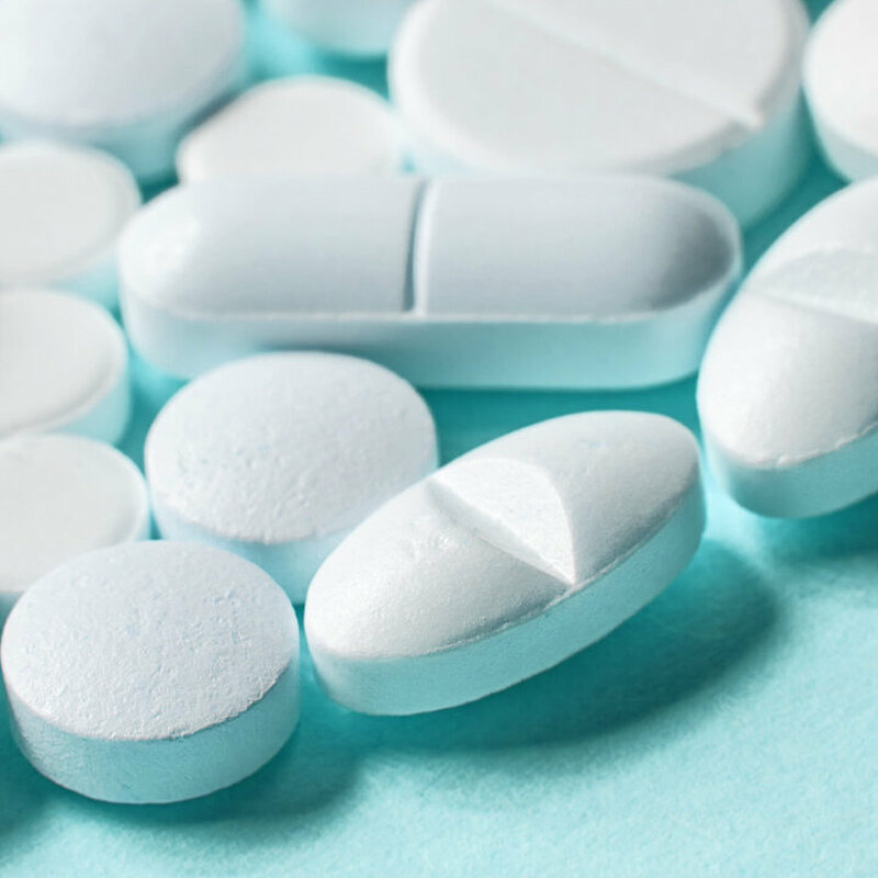 Weiße Pillen verteilt auf blauem Untergrund.