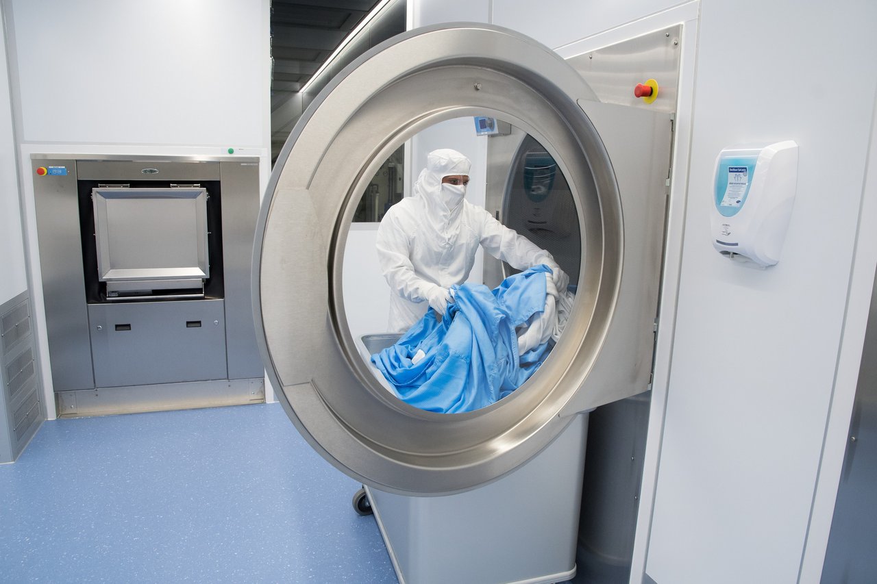 Waschmaschinen haben eine Durchladefunktion zum sicheren Einschleusen der Textilien. sie werden durch einen Mitarbeiter in Schutzkleidung befülltReinigung im Reinraum entladen